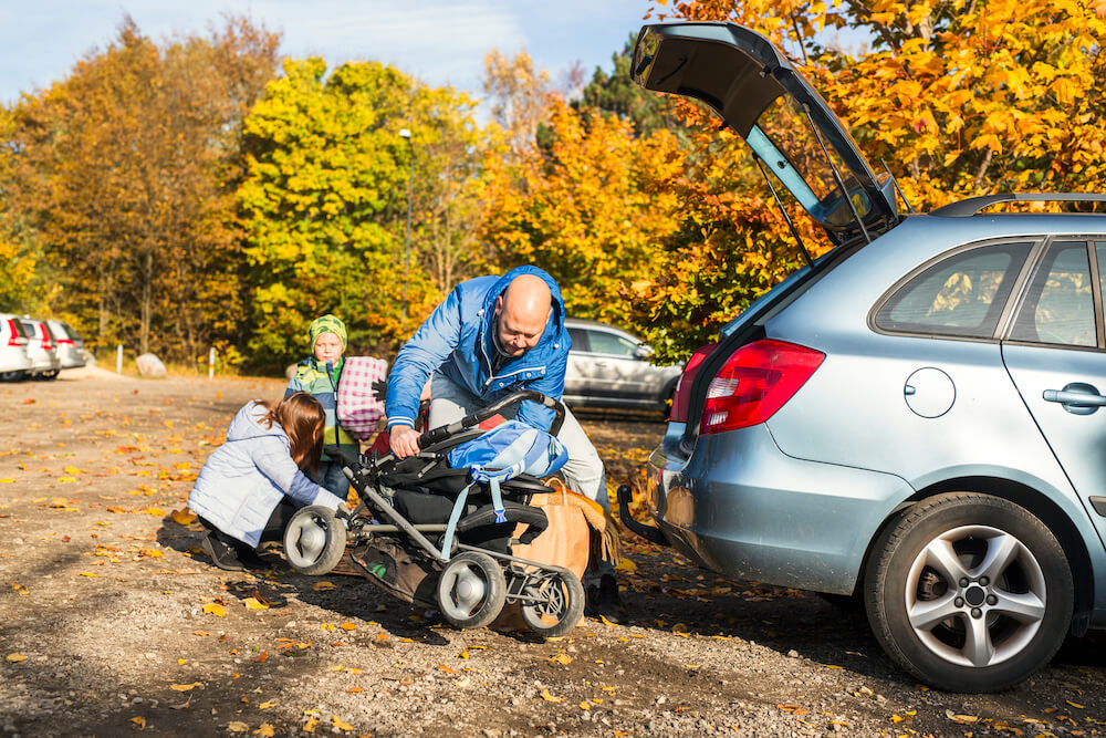 mann hebt kinderwagen in großen kofferraum