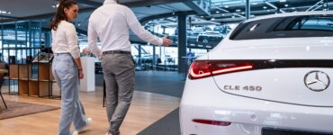 Frau geht mit Autohändler an einem Auto vorbei